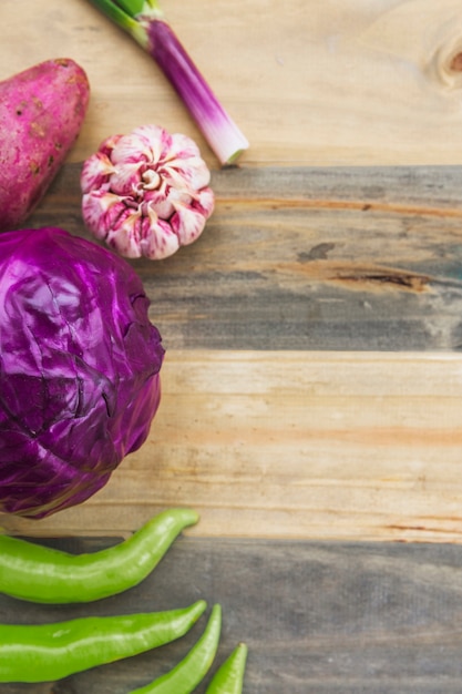 Vue grand angle du piment vert; chou rouge; ail et patate douce sur une planche en bois Photo gratuit
