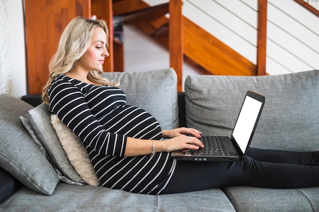 Vue latérale d'une femme enceinte à l'aide d'un ordinateur portable avec un écran blanc blanc Photo gratuit