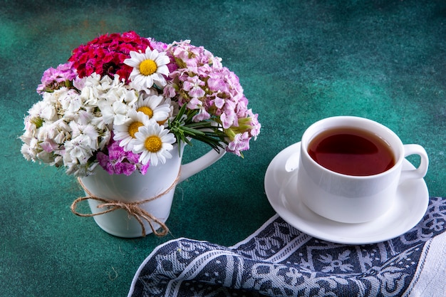 Vue Latérale Des Fleurs Colorées Dans Une Tasse Avec Une Tasse De Thé Sur Un Torchon Sur Vert 