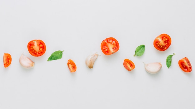 Vue panoramique de la moitié et de la tranche de tomates cerises; gousses de basilic et d'ail sur fond blanc Photo gratuit