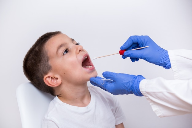 Vue rapprochée, le médecin met les mains dans des gants à l'aide d'un coton-tige pour tester les infections bactériennes du jeune garçon. Photo Premium