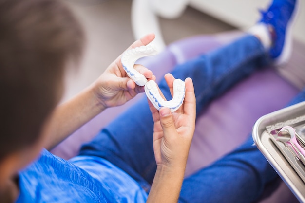 Vue surélevée de la main d'un garçon tenant un moule en plâtre pour les dents Photo gratuit