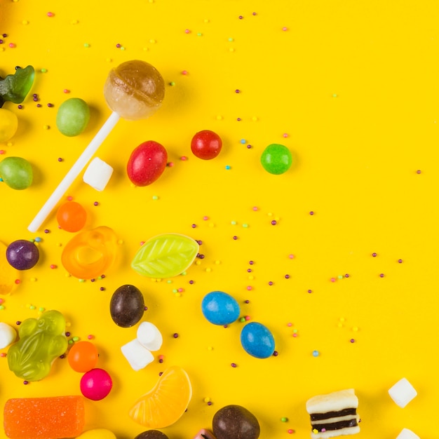 Vue surélevée de sucette et bonbons sur fond jaune Photo gratuit