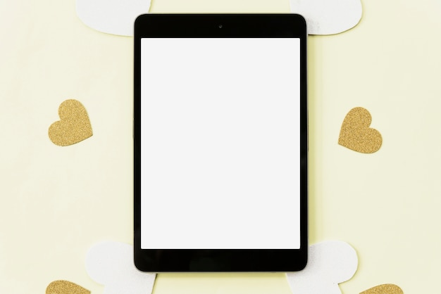 Vue surélevée de tablette numérique entourée d'autocollant de coeur sur fond jaune Photo gratuit