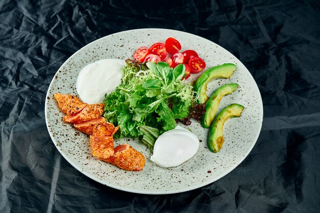 Insalata Gourmet Con Salmone Arrosto Salsa Di Panna Avocado Spinaci Lattuga Mozzarella E Pomodorini Sul Nero Insalata Di Mare Deliziosa Avvicinamento Foto Premium