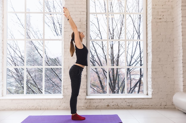 Ragazza Di Yoga Da Solo Nella Stanza Di Yoga Dalla Finestra Al Mattino In Piedi Con Le Mani In Alto Foto Premium