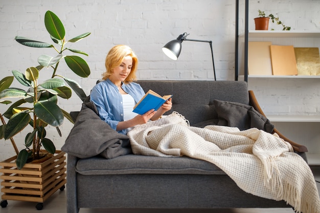 Giovane Donna Sotto Una Coperta Leggendo Un Libro Sul Divano Giallo Accogliente Soggiorno Nei Toni Del Bianco Foto Premium