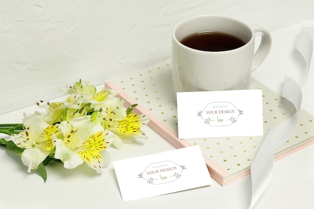 Mockup carte di carta su sfondo bianco con bellissimi fiori, note, nastro e tazza di caffè Psd Premium