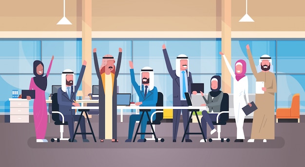 Groupe de gens d'affaires arabe joyeux tenue heureuse main levée mains assis au bureau bureau travailleurs musulmans succès Vecteur Premium