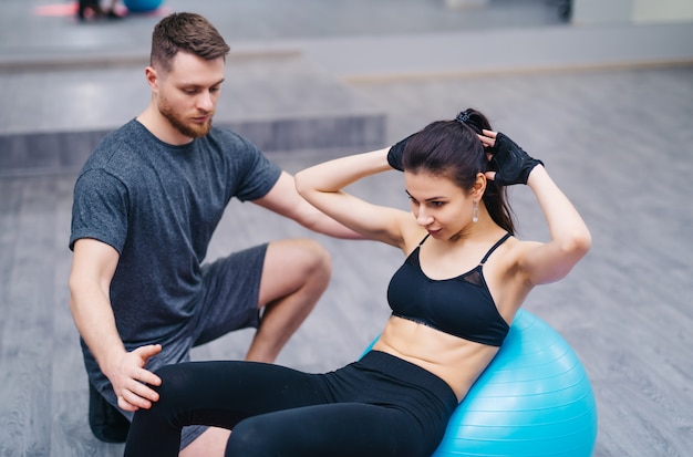 Aantrekkelijke jonge vrouw die abs op een geschiktheidsbal doet met persoonlijke trainer op de vloer in gymnastiek. Premium Foto