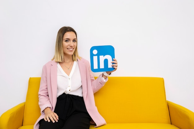 Aantrekkelijke jonge vrouw zittend op de bank holding linkedin pictogram Gratis Foto