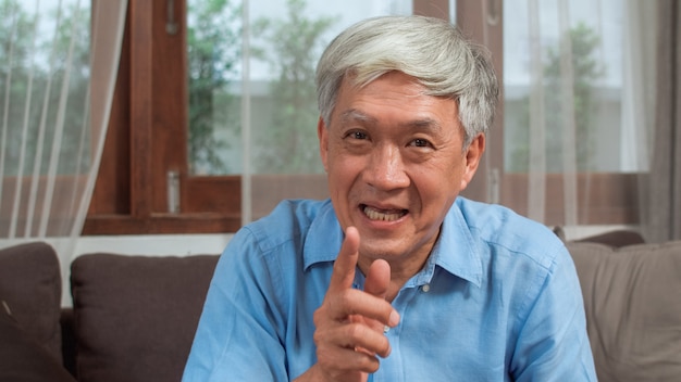Aziatisch hoger mensen videogesprek thuis. aziatisch hoger ouder chinees mannetje die mobiel telefoonvideogesprek met behulp van die met de kinderen van het familiekleinkind spreken terwijl thuis het liggen op bank in woonkamerconcept. Gratis Foto