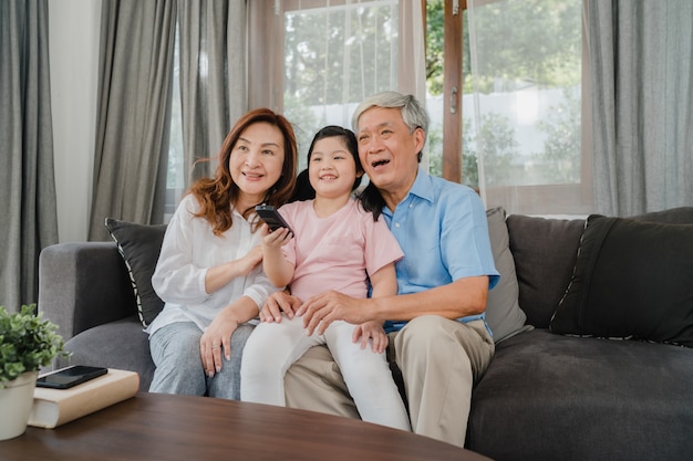 Aziatische grootouders kijken thuis tv met kleindochter. de hogere chinese, grootvader en grootmoeder gelukkige gebruikende familietijd ontspant met jong meisjesjong geitje liggend op bank in woonkamerconcept. Gratis Foto