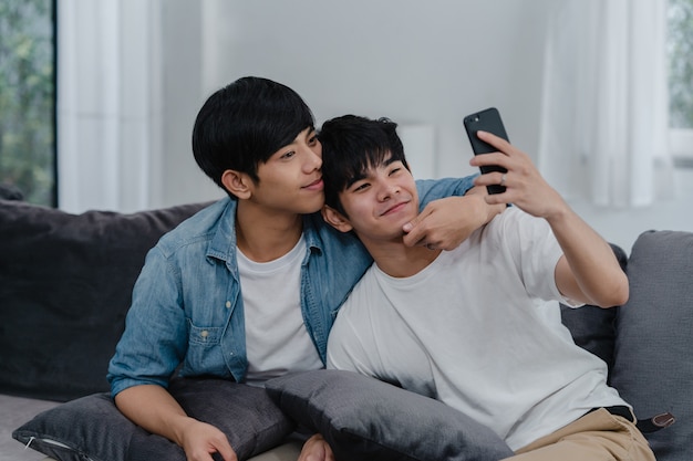 Aziatische influencer homopaar vlog thuis. aziatische lgbtq mannen gelukkig ontspannen plezier met behulp van technologie mobiele telefoon record levensstijl vlog video-upload in sociale media terwijl liggend bank in de woonkamer. Gratis Foto