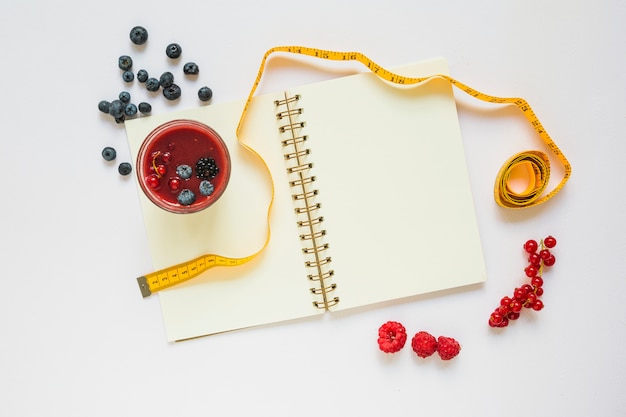 Bessen; smoothie glas; meetlint en spiraal notebook op witte achtergrond Gratis Foto