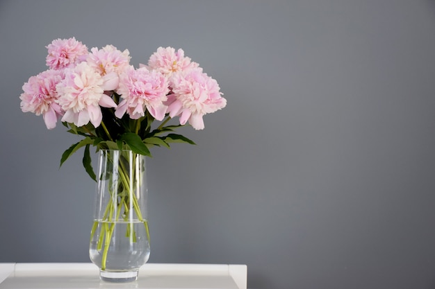 Boeket van pastel roze pioen bloemen in bloei in glazen vaas op witte