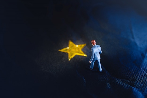 Bovenaanzicht van een miniatuur zakenman permanent op een gele gouden ster Premium Foto