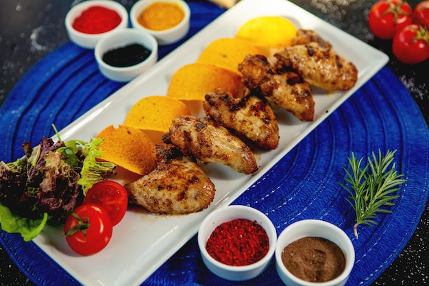 Bovenaanzicht van gegrilde kippenvleugeltjes geserveerd met gebakken aardappelen en verse salade Gratis Foto