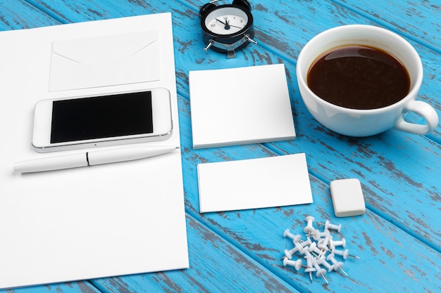 Branding kantoorbehoeftenmodel op blauw bureau. bovenaanzicht van papier, visitekaartje, notitieblok, pennen en koffie. Premium Foto