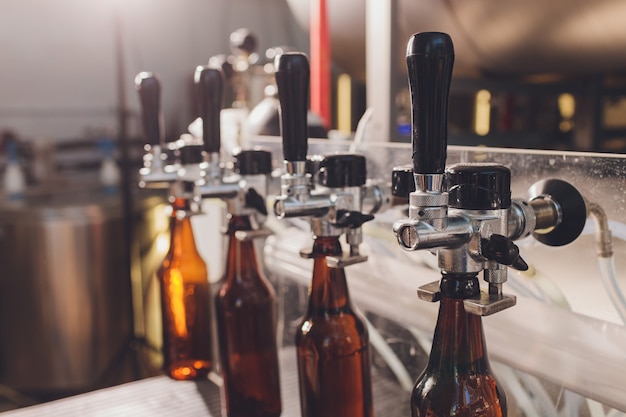 Brouwerijfabriek morsen bier in glazen flessen op transportbanden. industrieel werk, geautomatiseerde productie van eten en drinken. technologisch werk in de fabriek. Premium Foto