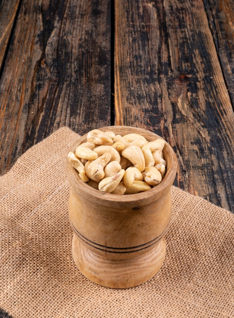 Cashew in een houten kop zijaanzicht op een stuk zak Gratis Foto