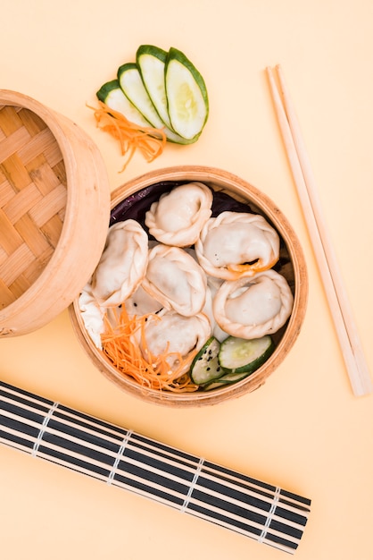 Chinese bol en salade in een doos van de bamboestoomboot op gekleurde achtergrond met eetstokjes Gratis Foto