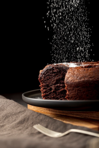 Chocoladecake met suikerpoeder wordt bestrooid op een zwarte plaat die Gratis Foto