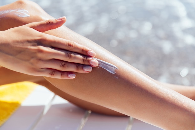 Close-up beeld van vrouwelijke hand zonnebrandcrème toe te passen op haar been, in de buurt van de zee. Gratis Foto