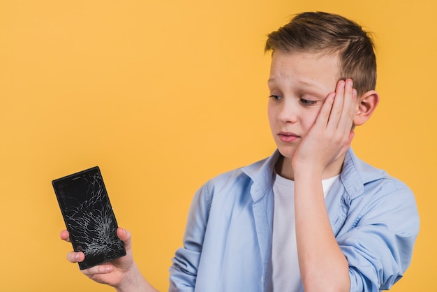 Close-up van boos jongen op zoek naar gebroken scherm van de mobiele telefoon tegen gele achtergrond Gratis Foto