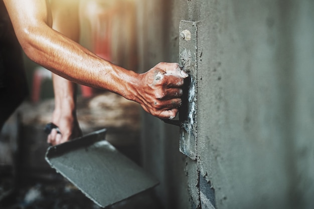 Closeuphand van arbeider het pleisteren cement bij muur voor de bouw