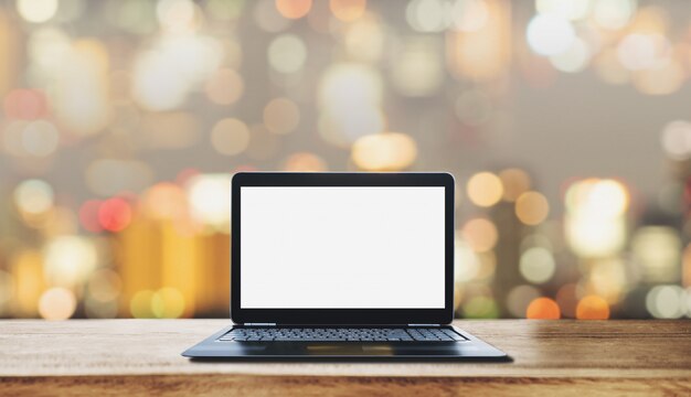 Computerlaptop het lege witte scherm op houten bureau, met de onscherpe lichte achtergrond van bokeh Premium Foto