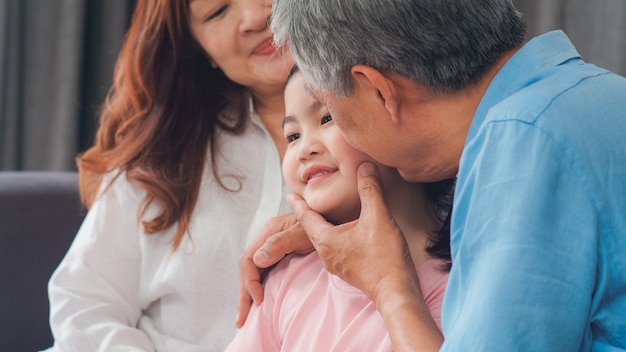 De aziatische grootouders kussen thuis de kleindochterwang. de hogere chinese, oude generatie, grootvader en grootmoeder die familietijd gebruiken ontspant met jong meisjesjong geitje liggend op bank in woonkamerconcept. Gratis Foto