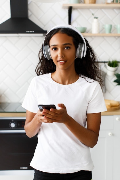 De jonge afrovrouw bevindt zich in de keuken en houdt een telefoon op