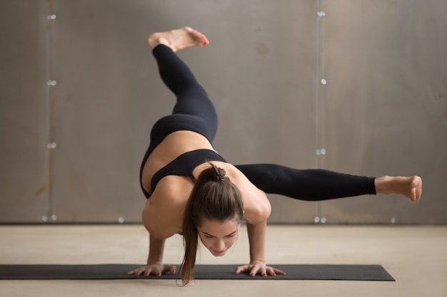 De jonge vrouw in eka pada koundinyasana 1 stelt, grijze studio Gratis Foto