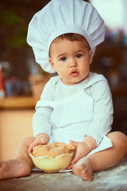 De kleine baby zittend op de tafel en spelen met deeg Gratis Foto