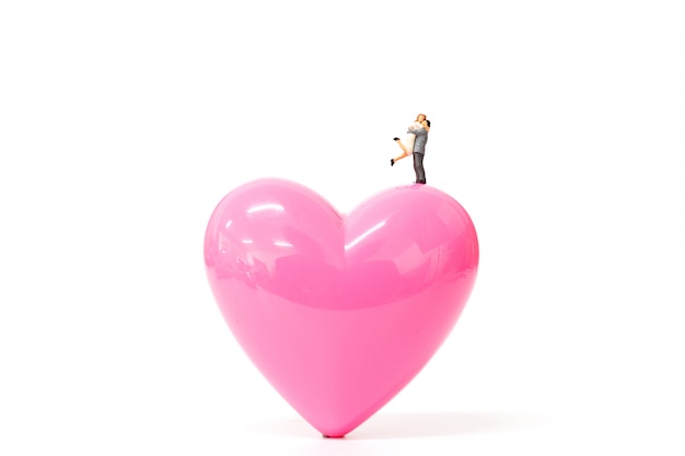 De miniatuurmensen koppelen aan roze hart op witte achtergrond Premium Foto
