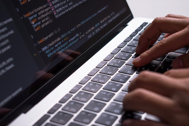 Detailopname. de hand van de ontwikkelaar maakt code op een computermonitor op een wit bureau. Premium Foto