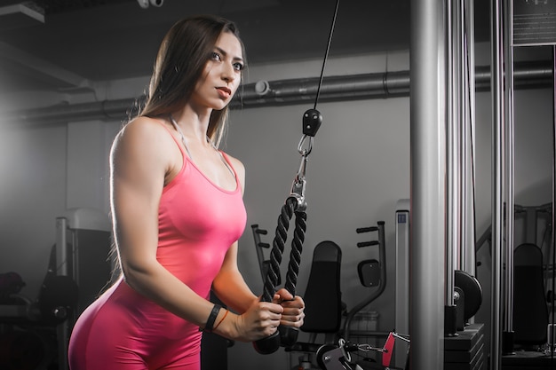 Donkerharige vrouw atleet in een trainingspak schudt hand-triceps biceps op een simulator in de sportschool. Premium Foto