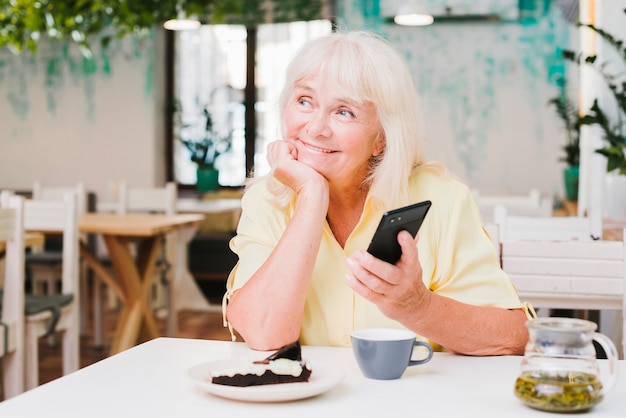 Dromerige glimlachende bejaarde met smartphone Gratis Foto