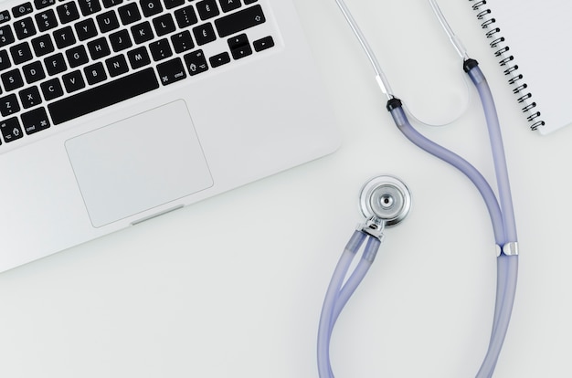Een bovenaanzicht van een laptop met een stethoscoop en spiraal notebook op witte bureau Gratis Foto