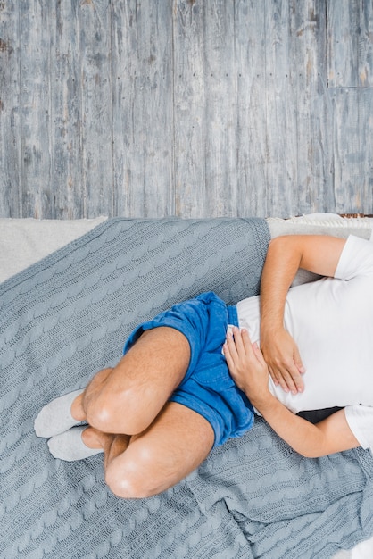 Een bovenaanzicht van een man met sok liggend op bed lijdt aan maagpijn Gratis Foto