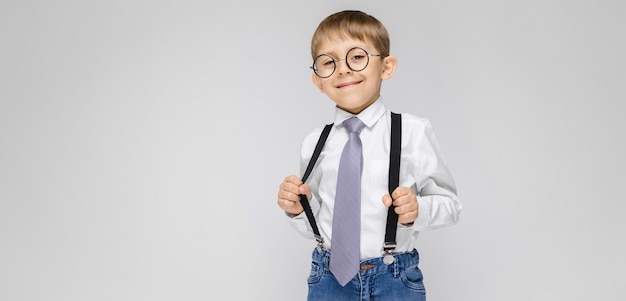 Besmettelijke ziekte Uitsluiting Sanders Een charmante jongen in een wit shirt, bretels, een stropdas en lichte  jeans staat. de jongen in glazen trok aan de bretels | Premium Foto