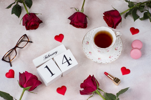 Een kopje thee, rode rozen, bitterkoekjes, satijnen harten, glazen en een kalenderdatum 14 februari Premium Foto