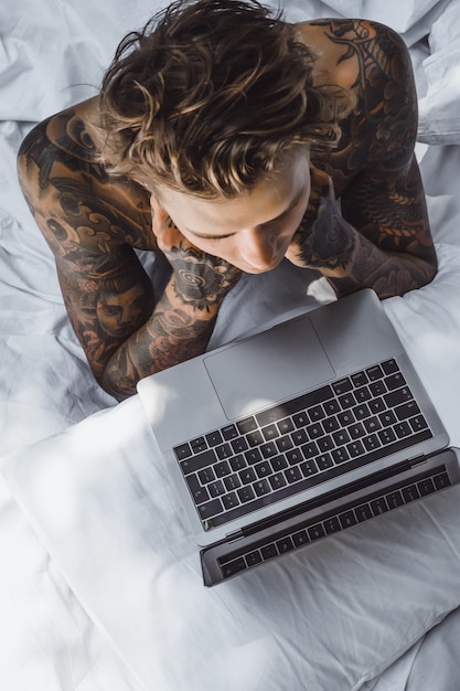 Een man in bed werkt op een laptop, post controleren, een kijken, naar muziek luisteren | Gratis Foto