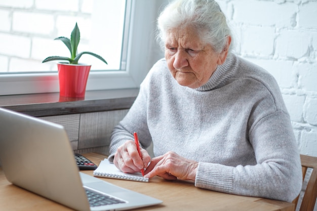 Een oude vrouw zit aan de tafel voor de laptop. Premium Foto