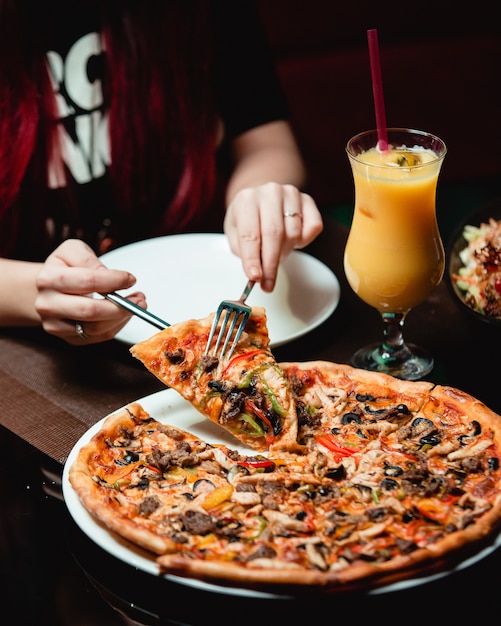 Een sneetje pizza met gemengd ingrediënt nemen met een glas sinaasappelsap. Gratis Foto