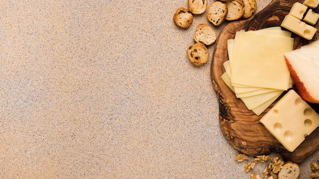 Emmentaler en gouda kaas met plakjes op coaster met sneetjes brood en walnoot over beige gestructureerde achtergrond Gratis Foto