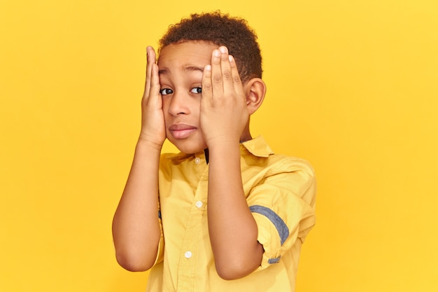 Emotioneel Kind Met Een Donkere Huid Dat De Handen Op Zijn Wangen Houdt Met Een Vergeetachtige Blik Van Streek Gestrest Vanwege Slechte Cijfers Op School Gratis Foto