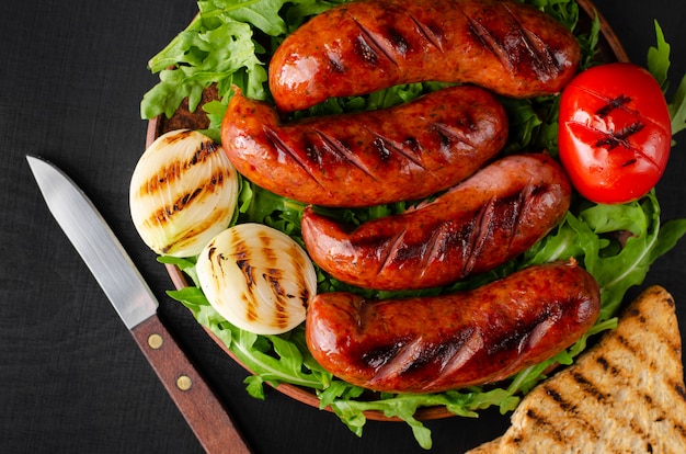 Gegrilde varkensworst met rucola en groenten op zwarte achtergrond. close-up, gereviseerd schot. Premium Foto
