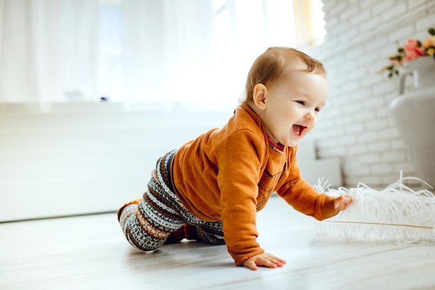 Gelukkig kind in oranje sweaterspelen met veer op de vloer Gratis Foto
